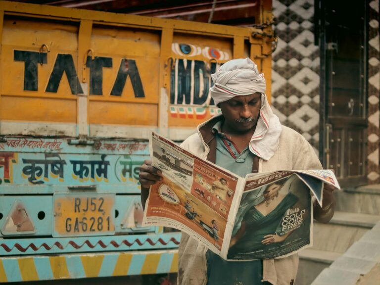 man reading newspaper standing behind dump truck
