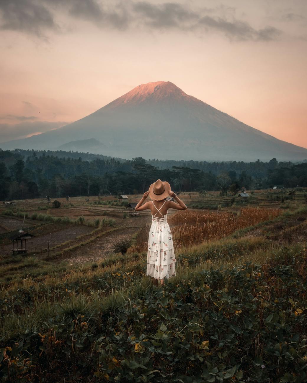 back view of a woman wearing white dress and sun hat standing on the farmland