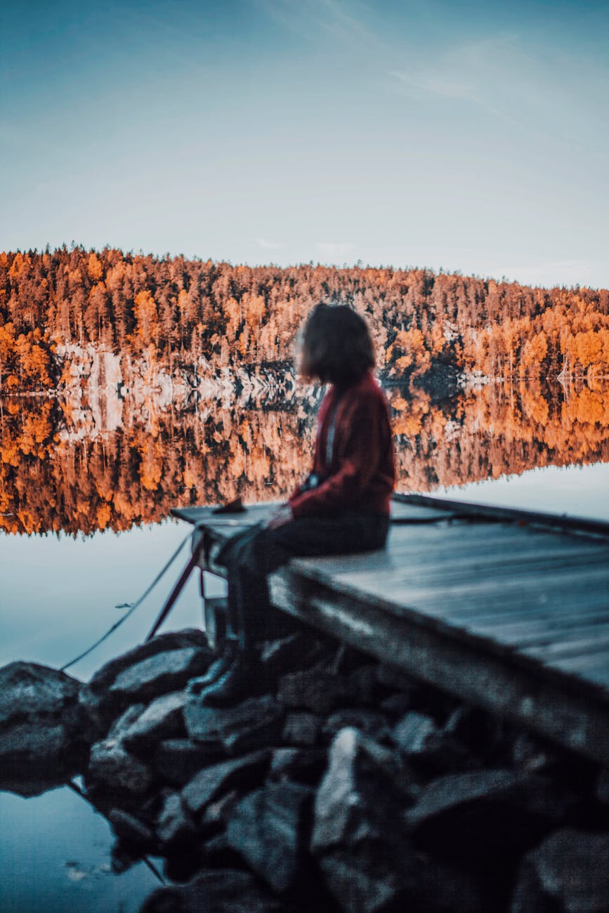 person sitting on wooden dock looking at the lake